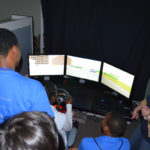 This is a photo of Houston Works USA students trying their skills on the TTI driving simulator.
