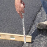 Person using tape measure to measure the depth of asphalt.