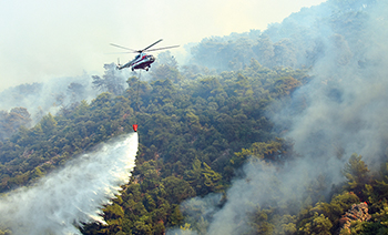 Firefighting helicopter in use over a forest fire in rough terrain.