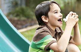 A boy sitting at the bottom of a playground slide using an inhaler.