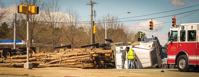 Emergency personnel near a timber truck on its side in a traffic intersection.