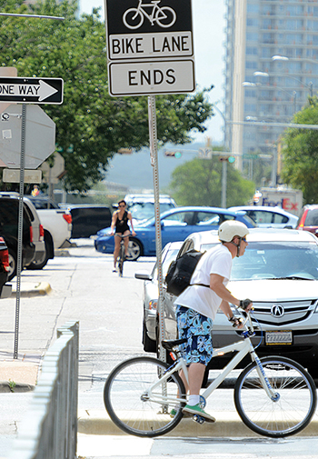 Car and bicycle traffic in an urban area with a 'Bike Lane Ends' sign displayed.