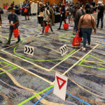 High School students participate in an interactive activity where they walk through a dummy intersection marked out on the floor.