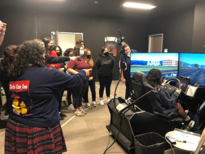 Students watching someone drive a driving simulator.