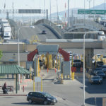 Photograph taken at a U.S.-Mexico border crossing showing passenger vehicle, truck, and pedestrian traffic.