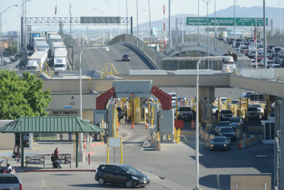 Photograph taken at a U.S.-Mexico border crossing showing passenger vehicle, truck, and pedestrian traffic.