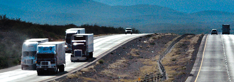 Freight trucks traveling I-10 in west Texas with mountains in the background.