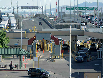 Photograph of a U.S.-Mexico border crossing.  Multiple forms of transport are being utilized: pedestrians, cars, and freight trucks.