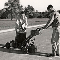 Historical photo of two men using striping equipment.