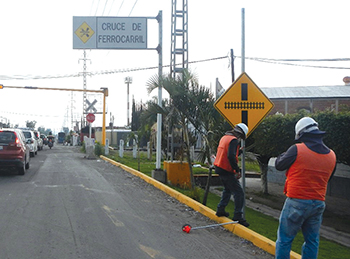 Workers installing a railway crossing intersection sign on a busy roadway in Mexico.