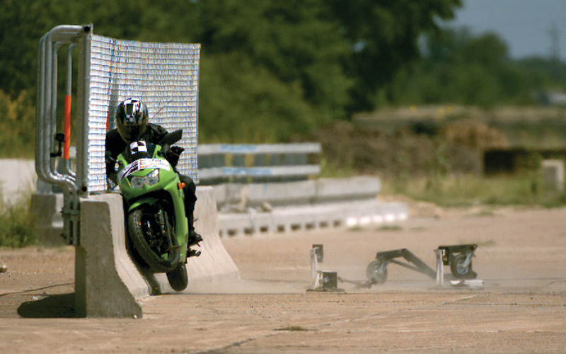 Crash test of a motorcycle roadside safety feature.  The photograph, taken during impact, shows the interaction of the test dummy and motorcycle with the net system attached to a concrete barrier.