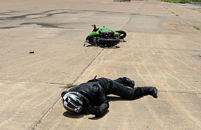 After impact with a barrier net system, the motorcycle and crash test dummy lie on the pavement.