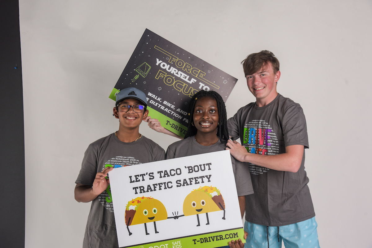 Teens at the 2023 Youth Transportation Safety Summit pose in front of the camera with signs displaying safety messaging.