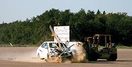 Small car crashing into a type III barricade during a test at the TTI Proving Grounds.