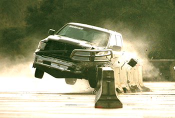 Pickup interacting with a concrete barrier with drainage structures during a crash test. 