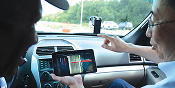 TTI researchers inside of a car looking at a handheld display showing simulated CVs during an HITL simulation.