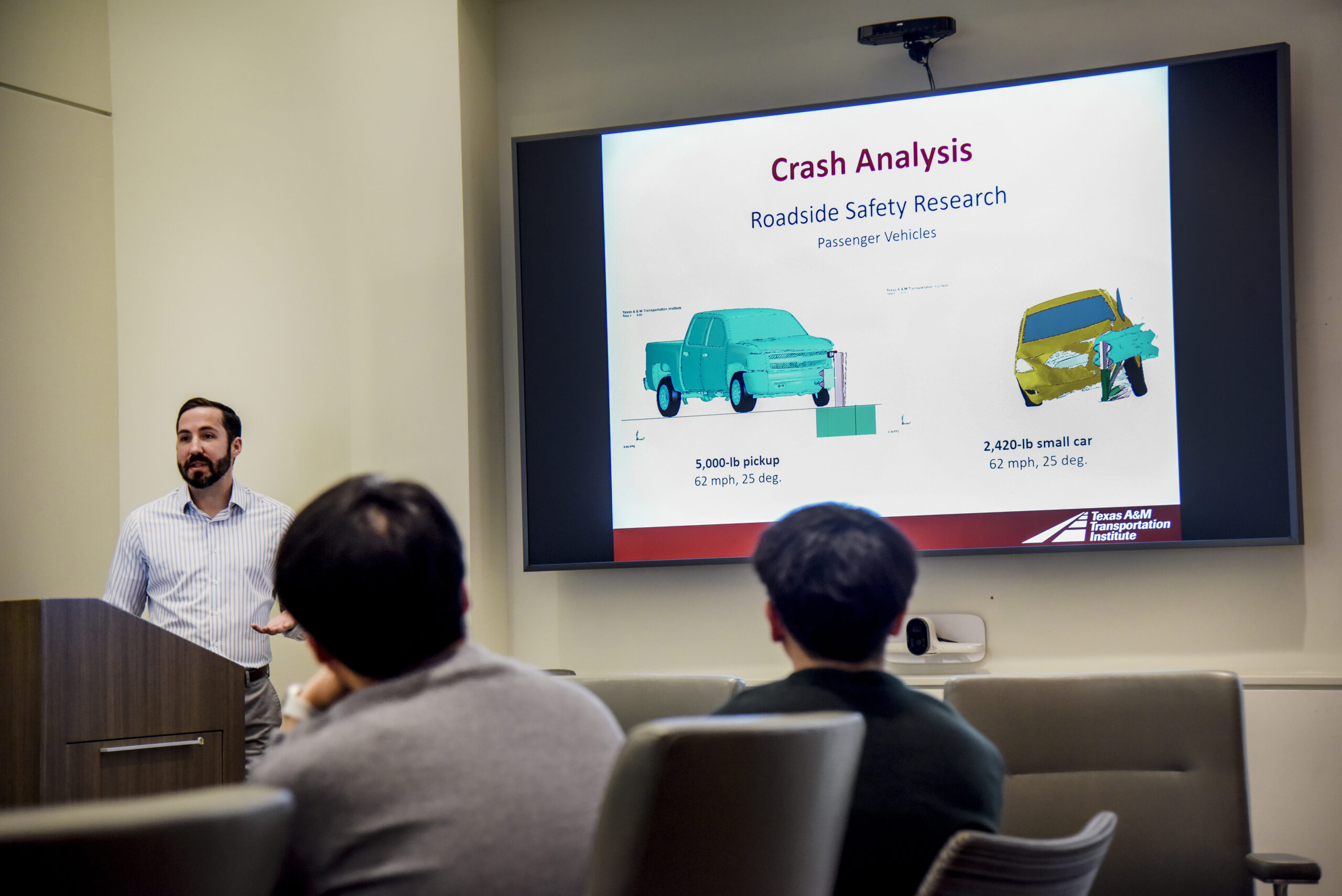 Nathan Schulz stands at the podium presenting information about crash analysis to visitors from the KAIST Program.