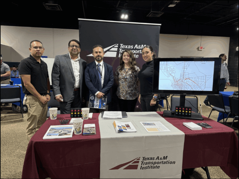 Five people stand behind a Texas A&M Transportation Institute booth with brochures, papers, and a screen displaying a city map.