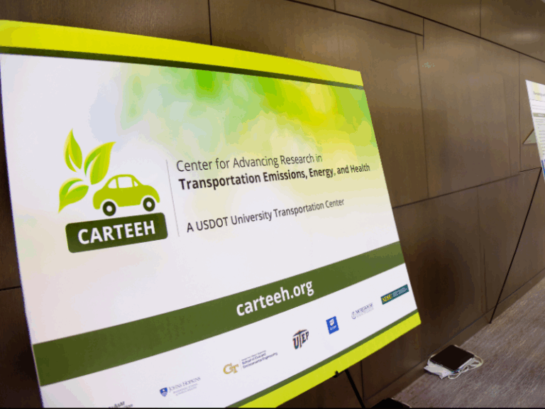 A poster for CARTEEH, the Center for Advancing Research in Transportation Emissions, Energy, and Health, is displayed against a wood-paneled wall.