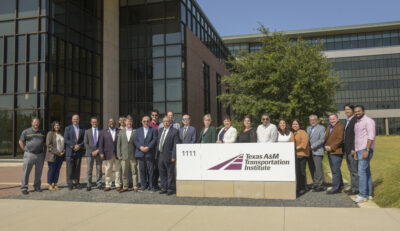 Group photo behind TTI logo and sign out front of the headquarters building.