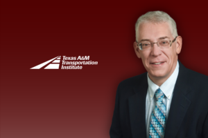 A man in a suit and tie poses in front of a maroon background with the Texas A&M Transportation Institute logo.