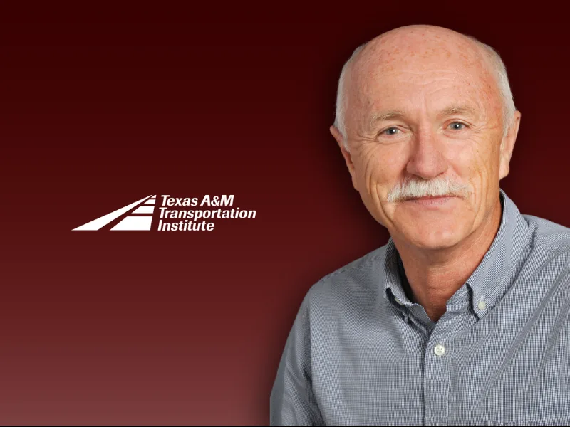A man with a mustache and gray hair wearing a button-up shirt poses in front of a maroon background with the Texas A&M Transportation Institute logo.