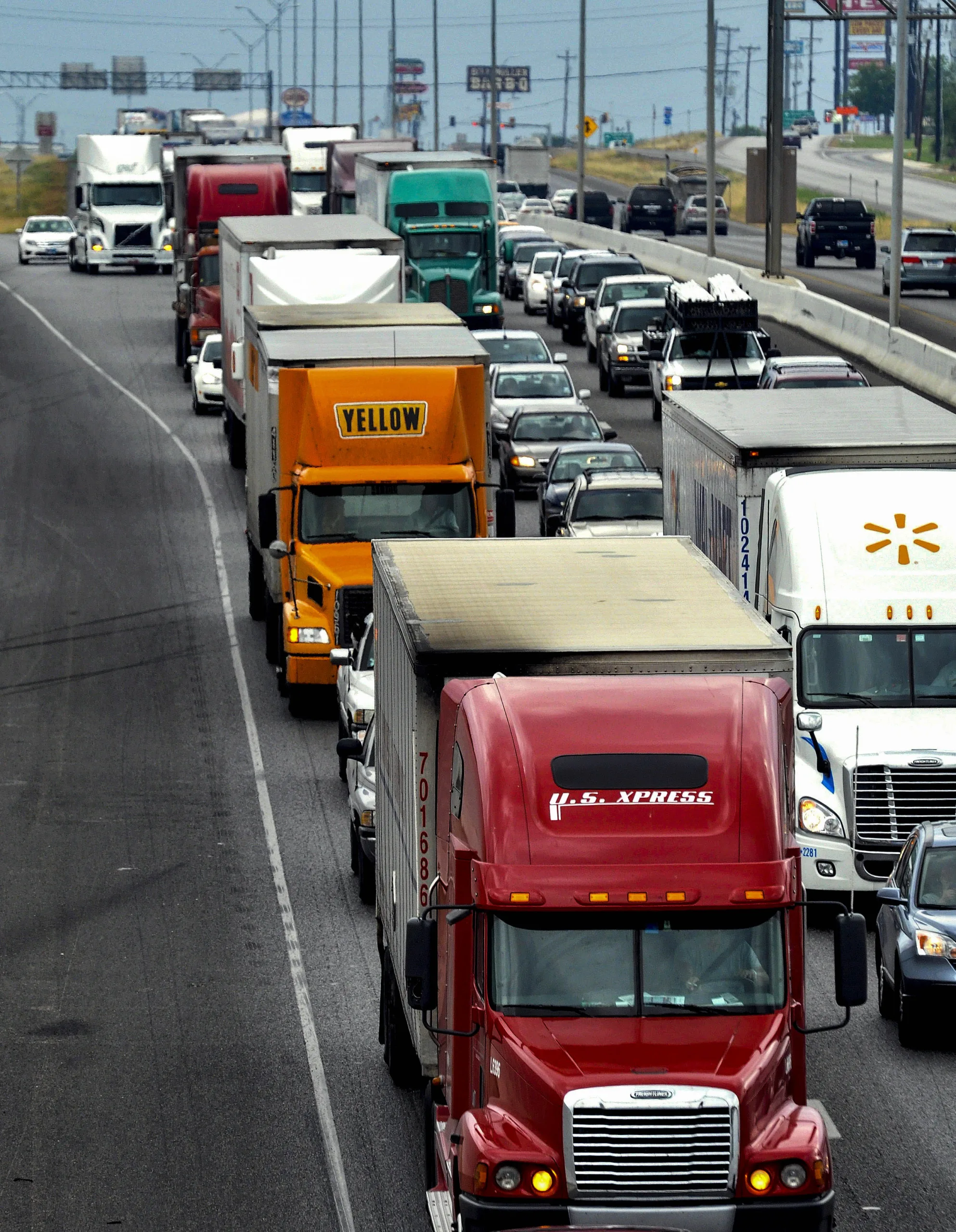 Multiple semi-trucks and cars are lined up in heavy traffic on a multi-lane highway during the daytime.