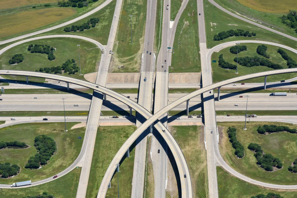 Aerial view of a multi-layer highway interchange with overpasses, cars, green grass, and trees surrounding the roads.