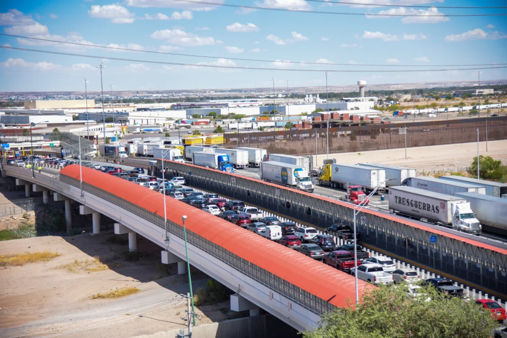 Aerial view of heavy traffic congestion on a border bridge with trucks and cars in separate lanes; industrial area in the background.