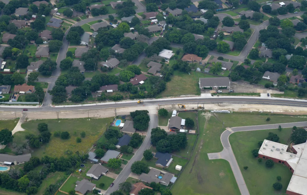 Aerial view of a suburban neighborhood with a road under construction cutting through houses and green yards.