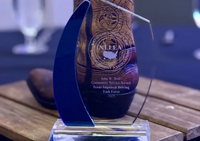 An engraved glass award in front of a decorative cowboy boot holding a red napkin.