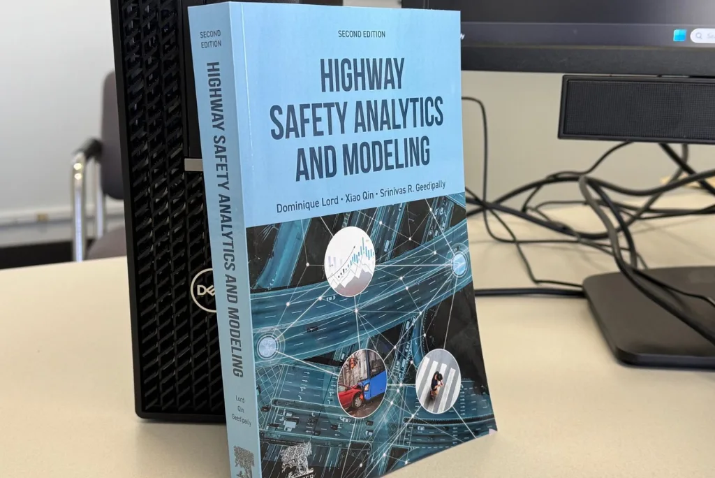 A textbook titled Highway Safety Analytics and Modeling stands upright in front of a computer monitor.