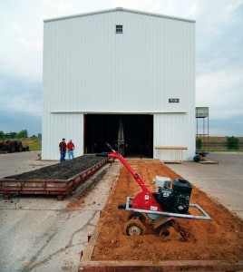 tiller in soil in front of large metal building